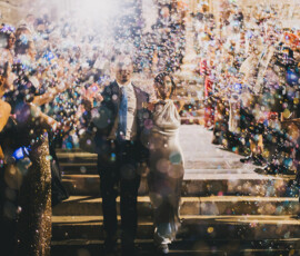 A newlywed couple descends steps as guests blow colorful bubbles at their joyful New Orleans wedding with festive lights.