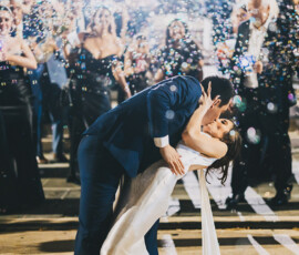 A couple in formal wear dip-kisses amid cheering guests and bubbles at a nighttime Gulf South wedding celebration.