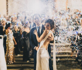 Bride and groom embrace at night in New Orleans, surrounded by cheering guests and sparkling confetti.