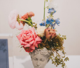 Head-shaped ceramic vase with pink, blue, and white flowers on a white indoor surface; stylish Louisiana wedding decor.
