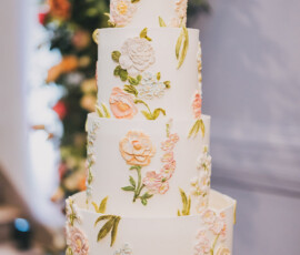 Elegant four-tier white wedding cake with pastel floral icing and green leaves, ideal for New Orleans weddings.
