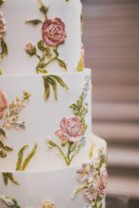 White tiered cake with colorful icing flowers, pink roses, and green leaves—ideal for a sophisticated Louisiana wedding.