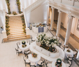 Elegant hall with white columns, floral tables, curved sofa, and flower-adorned grand staircase—ideal for Gulf South weddings.