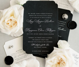 Black and white wedding invitations with white flowers, rings, and shoes on a light surface—timeless celebration style.