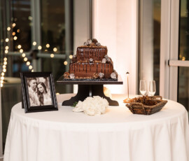 Wedding table in Orange Beach, AL with chocolate cake, couple photo, white flowers, treats, and string lights outside windows.