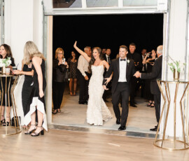 Bride and groom enter their Orange Beach Alabama wedding reception, smiling and waving as guests celebrate indoors.