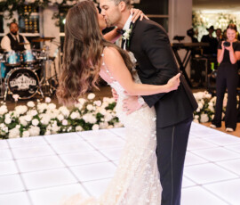 Bride and groom kiss during first dance on glowing white floor at Orange Beach, AL wedding with flowers, guests, and live band.