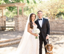 Bride and groom with their brown dog smile outdoors at their Orange Beach, Alabama wedding; trees and brick in the background.