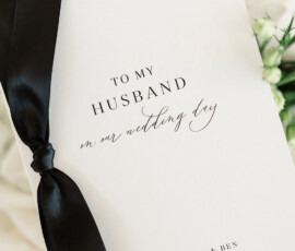 White wedding card with elegant script, black ribbon, pink and white flowers, dated Oct 26, 2024 from Mary Morgan & Ben.