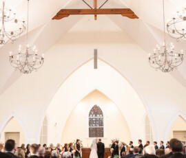 Bride and groom at altar in a bright church with vaulted ceilings, chandeliers, stained glass, and guests in Orange Beach, Alabama.
