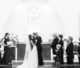 Bride and groom share first kiss at Orange Beach Alabama church altar, with wedding party, flowers, and stained glass.