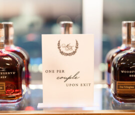 Woodford Reserve Double Oaked whiskey bottles with “The Fillings 10/26/2024” surround a “One per couple upon exit” sign.