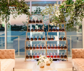 Chic lounge with beige sofas, glass coffee table, white flowers, bottle shelves, sunset windows, and hanging greenery.