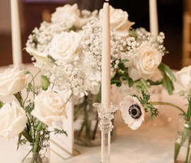 Elegant glass vases with white roses, baby’s breath, and anemones, plus three lit taper candles for an Orange Beach wedding.