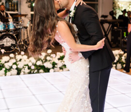 Bride and groom kiss while dancing on a white-lit floor at their Orange Beach, Alabama wedding, with white flowers and live band.
