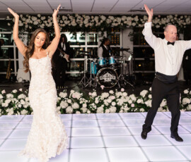 Bride and groom dance on a lit floor with live band and white flowers at an elegant Orange Beach Alabama wedding.