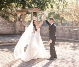 Bride and groom twirl and smile on a sunny brick patio at their Orange Beach Alabama wedding, surrounded by trees.