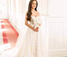 Bride in white lace dress with white rose bouquet in sunlit hallway at The Port, Orange Beach Alabama wedding.