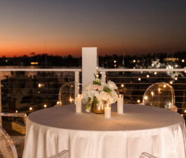 Elegant round table with candles and flowers on a balcony at sunset, marina view, perfect for an intimate Orange Beach wedding.