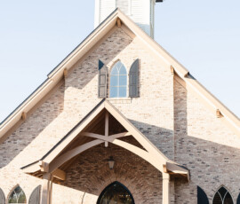 Brick church with arched windows, wreath-adorned doors, a peaked roof, and white steeple—ideal for Orange Beach or Gulf Shores weddings.