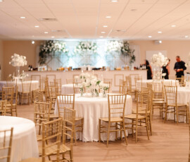 Chic banquet hall with white-clothed round tables, gold chairs, and floral centerpieces—ideal for Orange Beach weddings.
