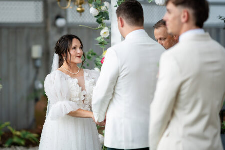 Bride and groom hold hands under a decorated arch at an outdoor Louisiana wedding ceremony, inspiring Gulf South weddings.