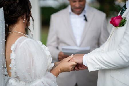 Bride and groom hold hands at their Louisiana wedding ceremony as the officiant reads from a paper in the background.