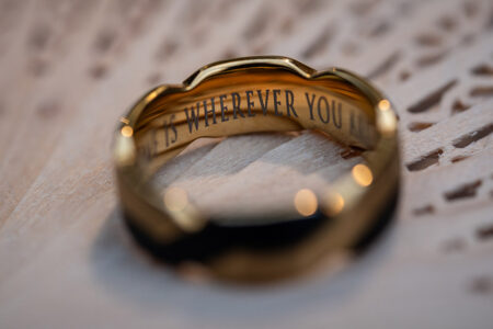 Gold ring engraved inside with “IS WHEREVER YOU,” ideal for a Louisiana wedding, on a light textured surface.