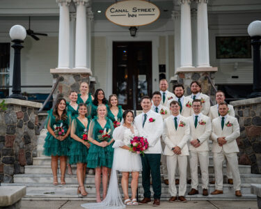 Wedding party on Canal Street Inn steps: bride in short white dress, groom and groomsmen in cream, bridesmaids in green.