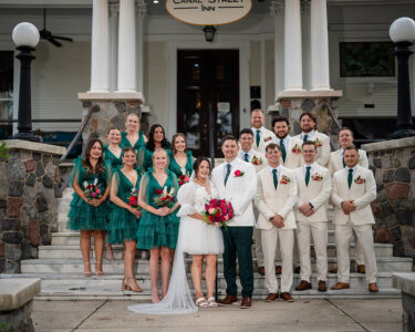 Wedding party on stone steps in Louisiana; bride in white, bridesmaids in green, groom and groomsmen in cream suits with green ties.