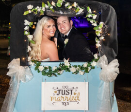 Newlywed couple smiles in a decorated blue car with Just Married sign, white flowers, and bows at night after their Louisiana wedding.