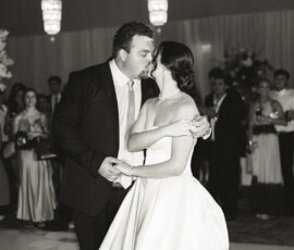 Bride and groom kiss while dancing at their Battle House Mobile wedding, surrounded by guests in a black and white photo.