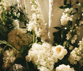 White and cream roses and hydrangeas with green leaves arranged before a white tablecloth, ideal for a Mobile Alabama wedding.