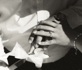 Black and white close-up of two people holding hands, one with a ring and bracelet—timeless Battle House Mobile wedding moment.