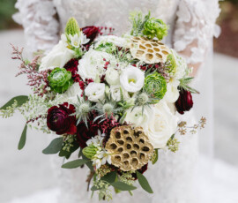 Bride in lace off-shoulder gown holding bouquet of white roses, red flowers, succulents at Cathedral Basilica Mobile wedding.