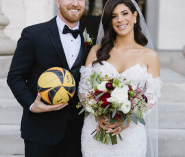 Bride in white dress and groom in black tuxedo with volleyball smile on stone steps after Cathedral Basilica Mobile wedding.