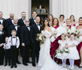 Bride with bouquet, bridesmaids in red, groomsmen in black, and children pose happily on stone steps at a Mobile wedding.
