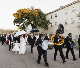 Bride, groom, flower girl, and guests parade with a brass band in Mobile, Alabama, celebrating outdoors with umbrellas.
