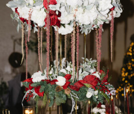 Elegant tall centerpiece with white hydrangeas, red flowers, and greenery on gold stands above a festive wedding table.