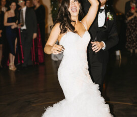 Bride twirls in white gown with smiling groom at elegant Crown Hall wedding in downtown Mobile, guests watching nearby.