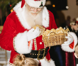 Santa Claus in a red suit gives a gift to a blonde girl at a festive indoor event, echoing lively wedding or holiday celebrations.