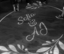Black and white photo of legs on a floor with “Sofia & AJ” projected in leafy design at a downtown Mobile wedding.