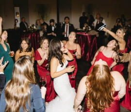Bride in white dress dances with laughing bridesmaids and guests at a lively Crown Hall wedding in downtown Mobile.