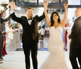 Newlyweds in formal attire walk out, hands raised and smiling, as guests cheer and hold sparklers after their Cathedral Basilica wedding.