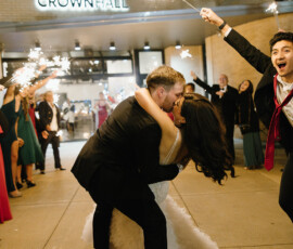 Newlyweds kiss during a sparkler exit at night, cheered by guests outside Crown Hall, celebrating their Mobile Alabama wedding.
