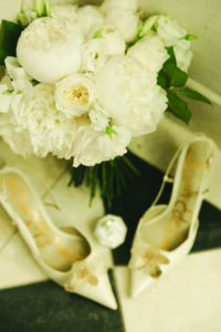 White flower bouquet and white high heels with gold accents on black-and-white tiles, elegant New Orleans wedding scene.