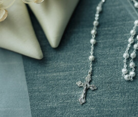 Silver rosary and ivory heels with floral accents on soft blue fabric, evoking classic Battle House Mobile wedding elegance.
