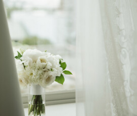 White flower bouquet in glass vase on a windowsill, framed by sheer curtains and soft natural light at Battle House Mobile wedding.