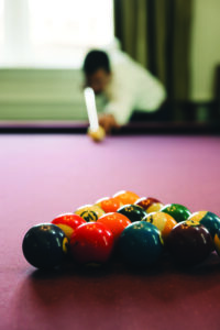 Billiard balls racked on a pool table with a blurred player aiming to break, highlighting a playful Gulf South wedding vibe.