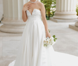 Bride in strapless white gown with pearl jewelry and bouquet, smiling by white columns at her Mobile, Alabama wedding.